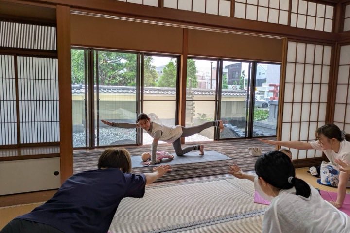 和室でのストレッチ・ヨガ教室で、赤ちゃんを前にした先生と同じポーズをとる参加者のようす