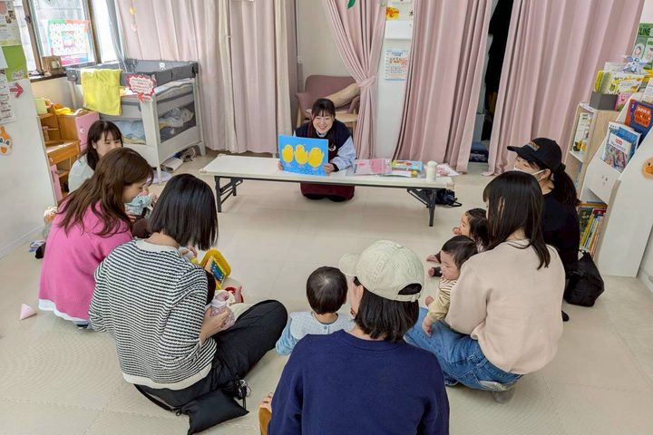 おでかけひろばで、赤ちゃんを抱いたママたちが絵本の読み聞かせを楽しむようす