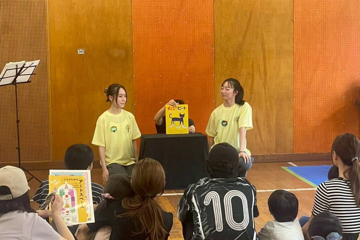 体育館で、一本の樹のスタッフが子どもたちに絵本を読んでいるようす